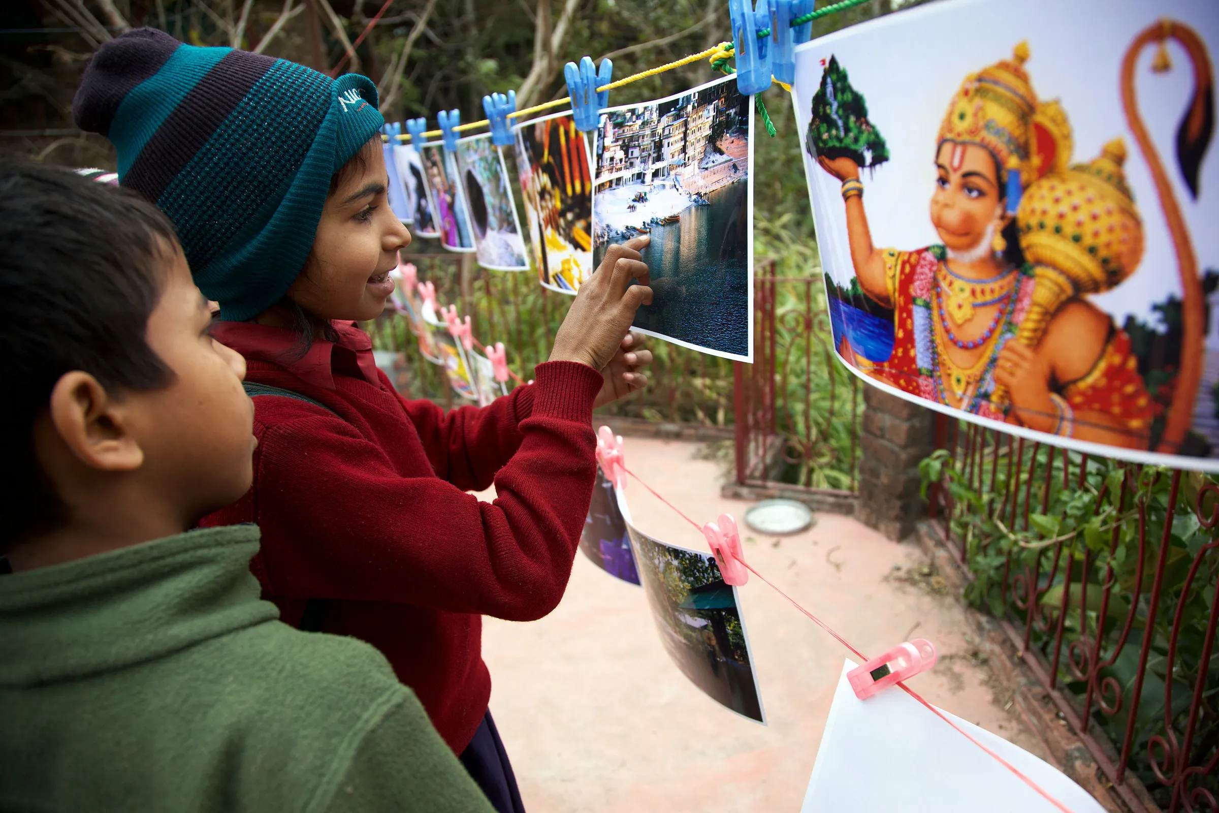 Children looking at printed photographs pegged to a line outdoors.