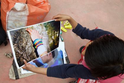 A child holding up a printed photograph of a hand resting on stone.