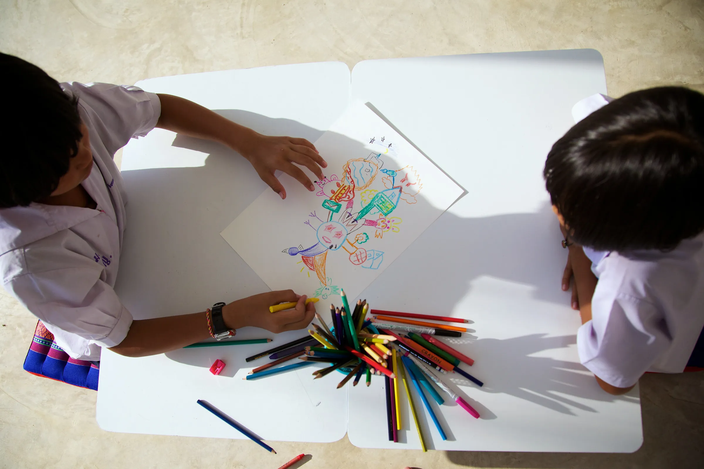 Two children seen from above drawing on one shared sheet, with the words Ping Pong Painting added over the photograph.