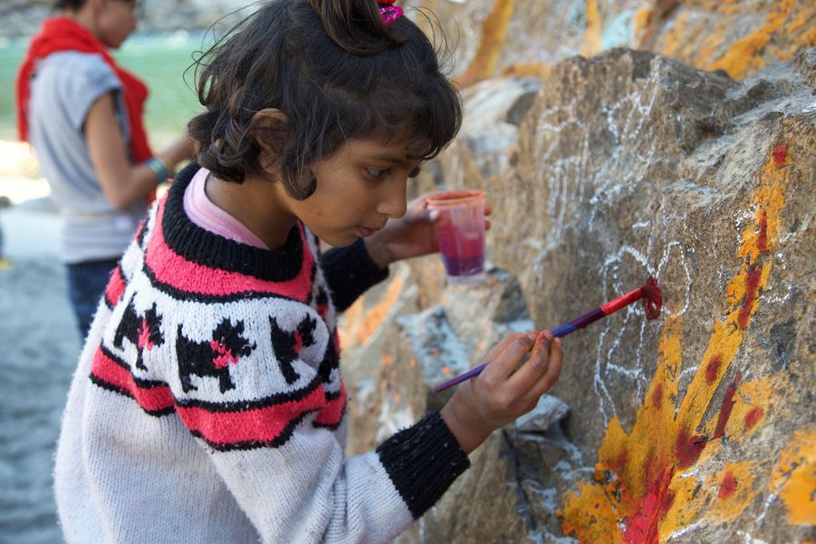 A child painting yellow and red onto a large rock.