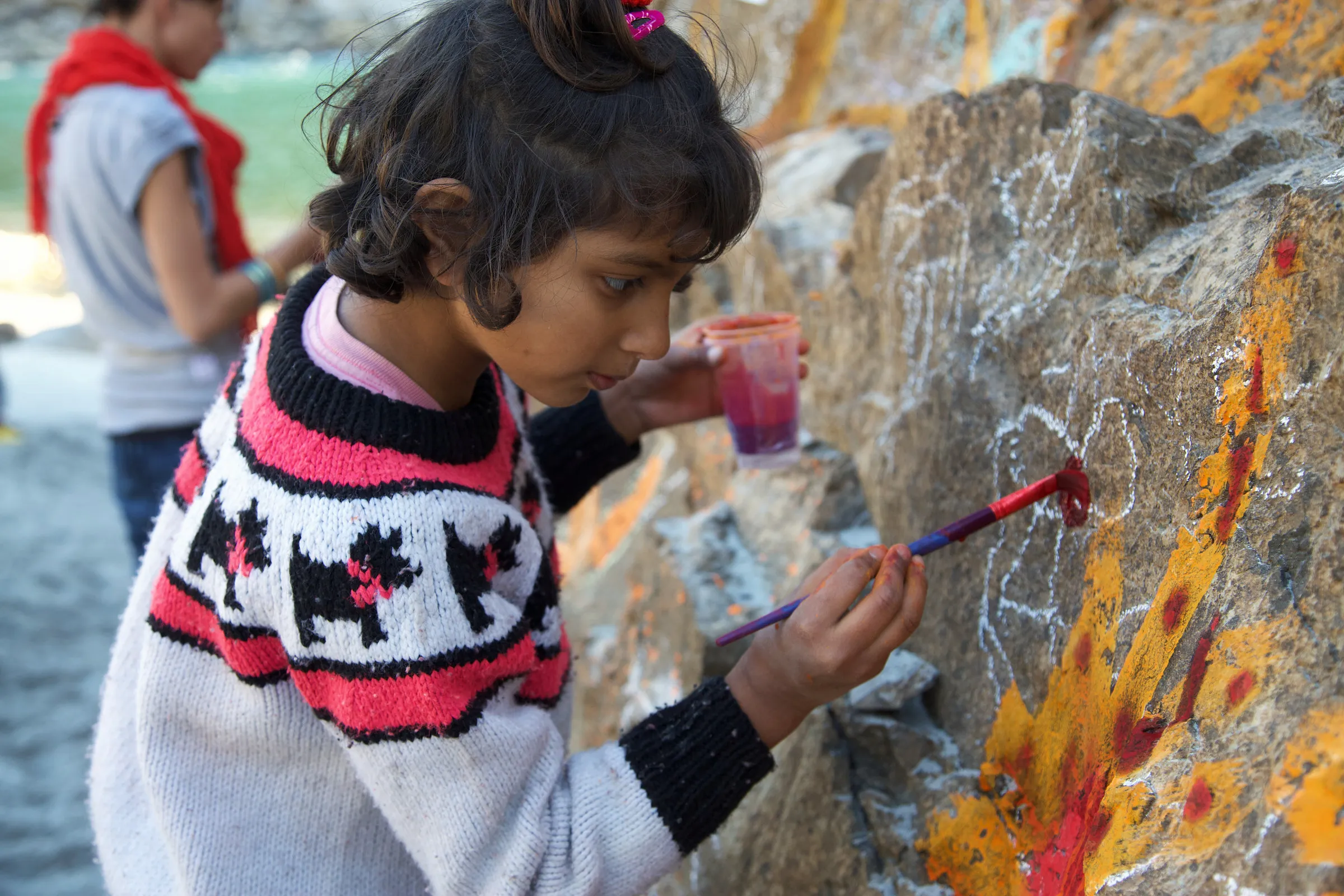 A child painting yellow and red onto a large rock.
