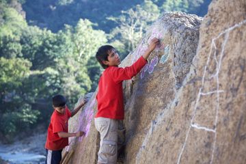 Two children drawing with chalk on a large rock face.