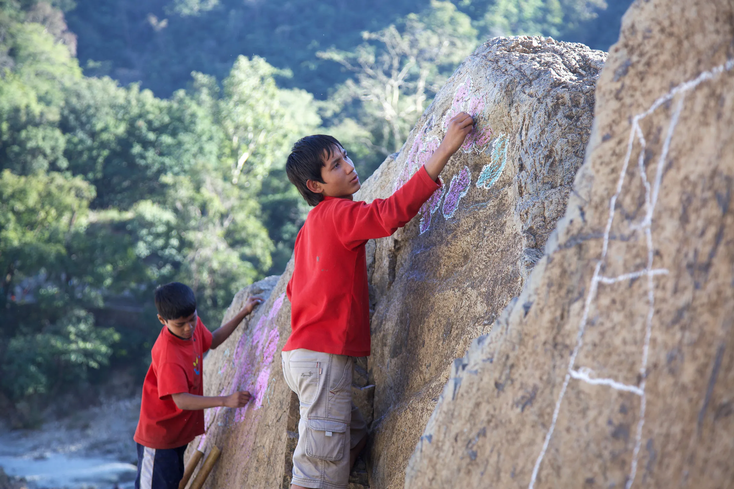 Two children drawing with chalk on a large rock face.