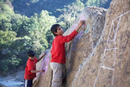 Two children drawing with chalk on a large rock face.