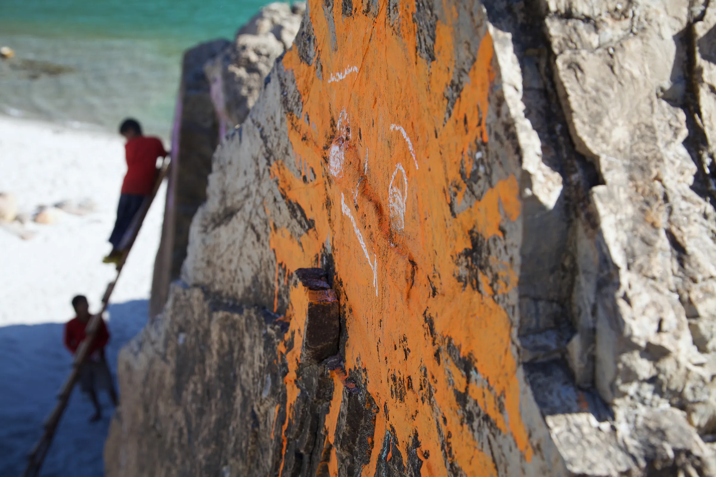 A large rock painted with an orange sun shape, with a person on a ladder nearby.
