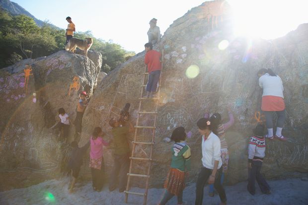 Children and adults drawing on large boulders in bright sun, one of them on a ladder.