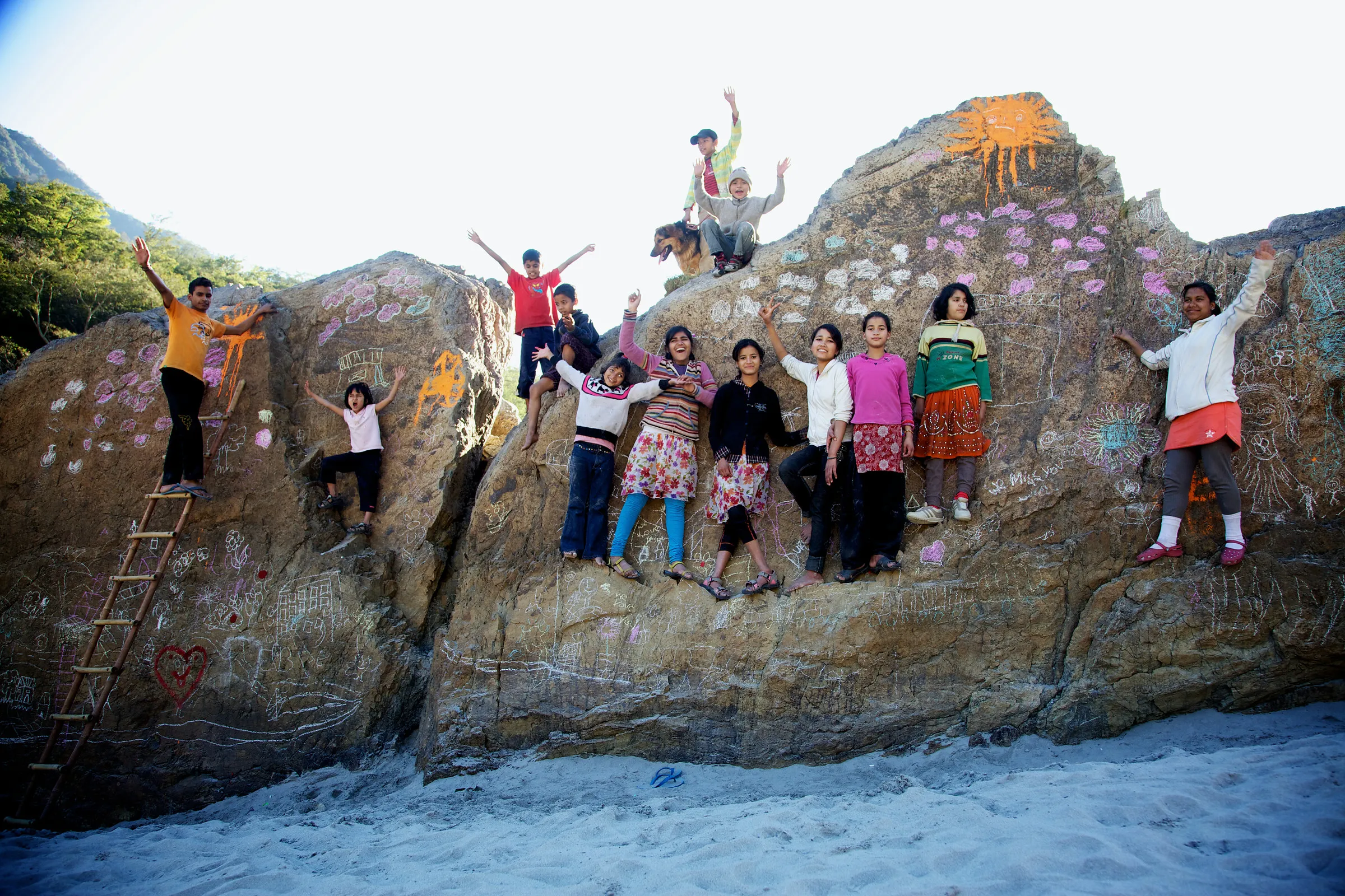A group standing along the base of a drawn-on boulder, some of them waving.