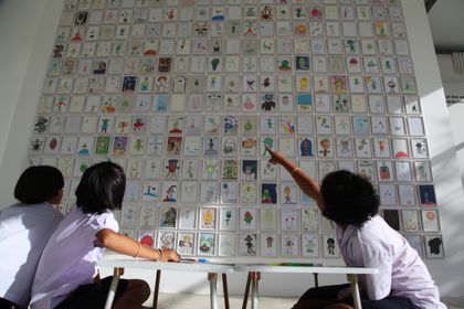 Children in front of a gallery wall covered with hundreds of alien drawings, one pointing at a drawing.
