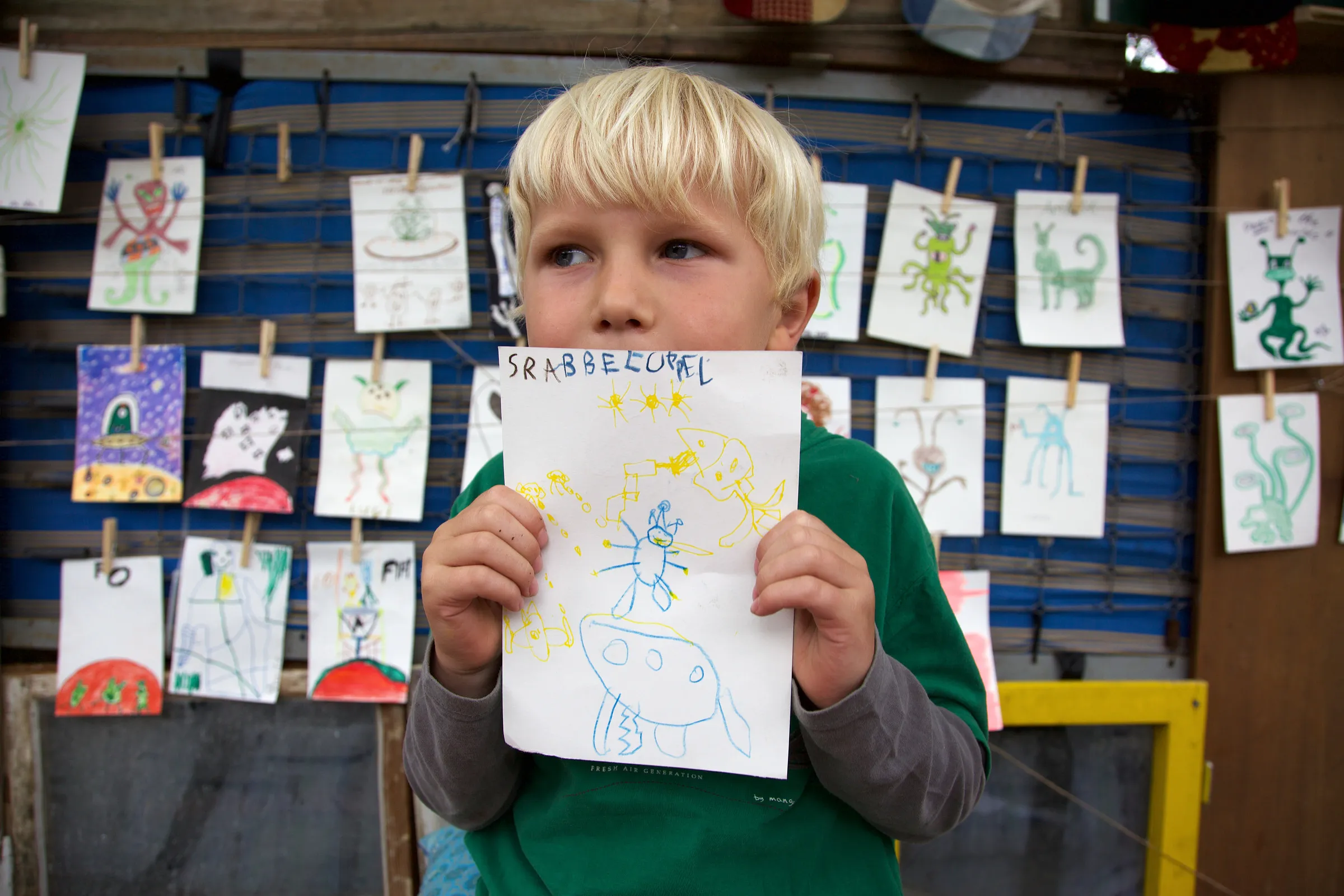 A child holding up an alien drawing in front of drawings pegged to a string.