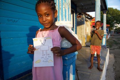 A child holding an alien drawing on a porch.
