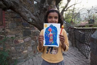 A child holding a colourful alien drawing on a stone path.